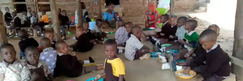 Kinder in Lupiro Tansania sitzen in der Schule aquf dem Boden und essen ihre warme Mahlzeit. (c) Reinhold Schlicker Kinder in Lupiro Tansania sitzen in der Schule aquf dem Boden und essen ihre warme Mahlzeit.